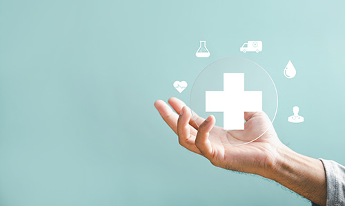 A hand holding floating healthcare icons, including a medical cross, heart monitor, ambulance, test tube, blood drop, and doctor symbol, on a light teal background.